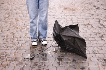 Woman and broken umbrella on wet pavement outdoors, closeup