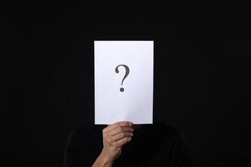 Man hiding behind paper sheet with question mark on dark background
