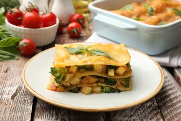 Piece of tasty vegetarian lasagna and ingredients on wooden table, closeup