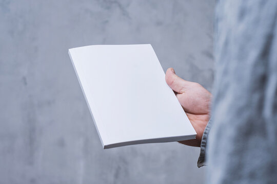 Realistic mockup of book cover, magazine in the hands of a man on concrete background. Concept for demonstrating editorial design, book covers and printed materials.
