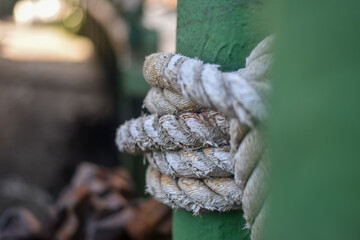 white rope on an iron pole. A thick white rope is wrapped around a green metal bollard, securing a...
