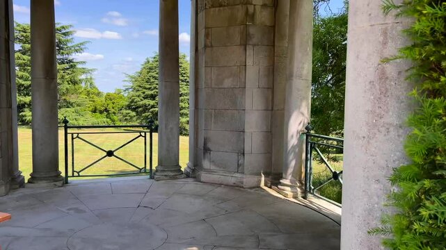 Garden pavilion framed by clipped green hedges and golden stone path beneath a blue English sky, traditional and timeless, slow motion