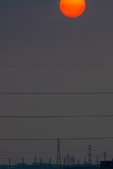 梅雨空に昇る太陽と鉄塔