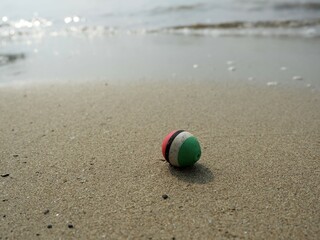 A colorful, striped fishing float, seemingly abandoned, resting on the sandy beach with gentle...