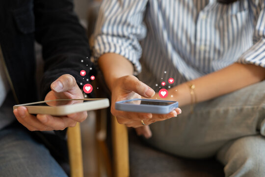 close up couple man and woman hold smartphone and using dating application to talk and make conservation and give love sign (heart) to each other while sitting together in cafe for romantic lifestyle
