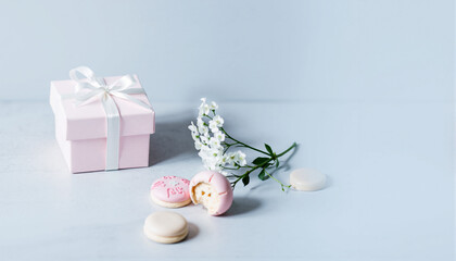 Elegant pastel-colored gift box with pink and white macarons, delicate white flowers, and a soft blue background creating a charming and sophisticated aesthetic