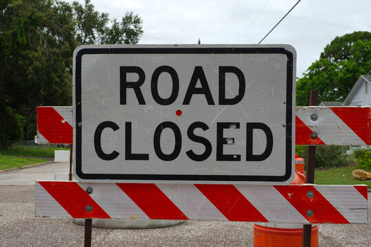 Road Closed Sign on Barricade in Outdoor Urban . Mounted on a barricade, illustrating a temporary road closure situation. The surrounding street and environment suggest construction or maintenance 