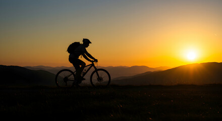 Silhouetted cyclist riding mountain bike during sunset on scenic outdoor trail with mountains in the background and vibrant sky creating a peaceful and adventurous atmosphere