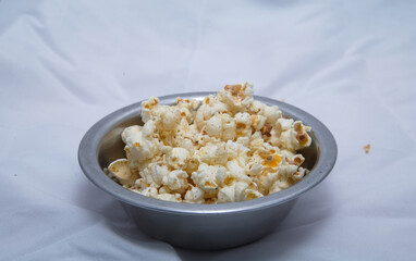 Popcorn in a bowl and TV game remote control isolated background. Wooden bowl of popcorn and remote control in the background the TV works. Evening cozy watching a movie or TV series at home.