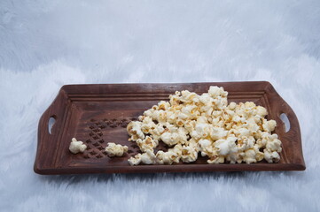 Popcorn in a bowl and TV game remote control isolated background. Wooden bowl of popcorn and remote control in the background the TV works. Evening cozy watching a movie or TV series at home.