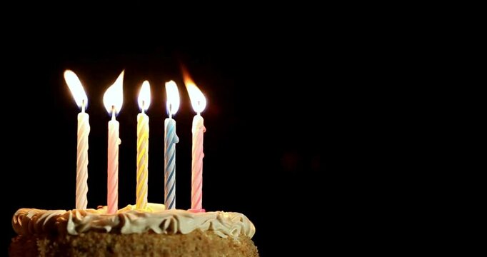 Close-up of lit candles on a birthday cake, with a black background and excellent quality