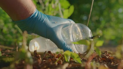 Hand in blue latex glove picking up plastic cup with milkshake remains from ground closeup slow motion environmental cleanup concept