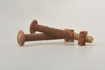 close-up of rusted bolts with nut attached isolated neutral gray background, reddish brown discolored and sings of heavy corrosion, selective focus