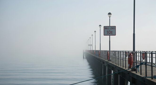 Pier Disappearing Into Mysterious Fog Over Water Landscape On A Calm Morning