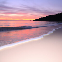 Fototapeta premium Beautiful Sunset over a Calm Beach with Gentle Waves and a Distant Mountain Silhouette
