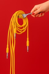 Bright yellow audio cables intertwined and held by a fork against a vibrant red background in a creative composition
