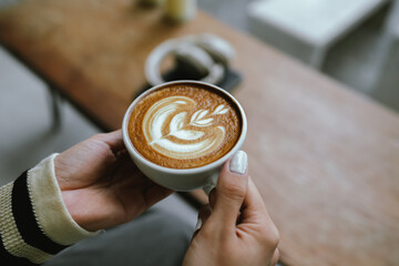 A beautifully presented latte in a white mug rests on a clean tabletop, inviting relaxation,...