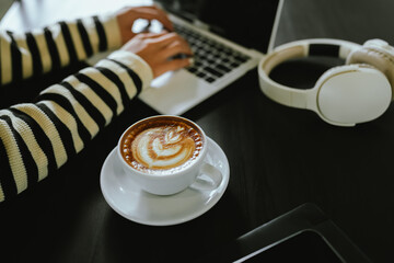 A cozy moment of balance and focus as a person enjoys a latte, checks their smartphone, and works...