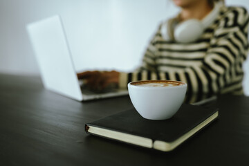 Young Asian woman making latte in a relaxed atmosphere with laptop and notebook and notepad while...
