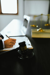 A gavel rests on a legal desk with blurred background of a professional signing documents, symbolizing justice, legal process, court authority, and formal legal consultation setting.