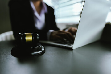 A gavel sits on a desk beside a laptop as a lawyer works, symbolizing the intersection of modern...