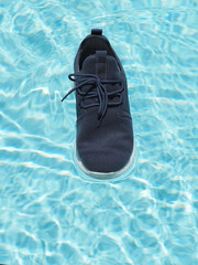Sneakers floating on a swimming pool surface under bright sunlight.
