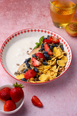 Plate with yogurt and muesli topped with fresh strawberries on pink background. Summer breakfast...