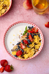 Plate with yogurt and muesli topped with fresh strawberries on pink background. Summer breakfast...