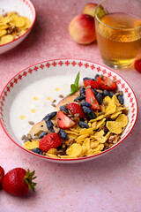 Plate with yogurt and muesli topped with fresh strawberries on pink background. Summer breakfast concept, light and refreshing morning meal.