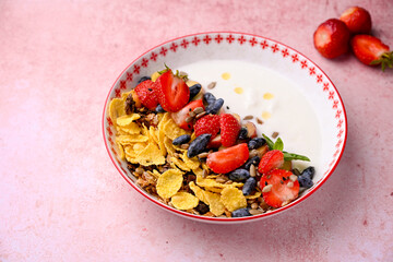 Plate with yogurt and muesli topped with fresh strawberries on pink background. Summer breakfast concept, light and refreshing morning meal.