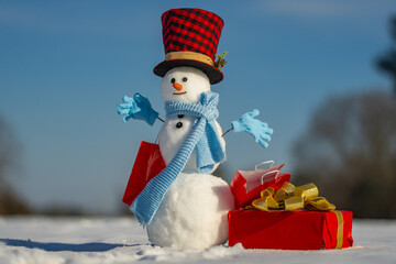 Snowman holding a gift present on winter background. Snowman with gift on a snowy winter day....
