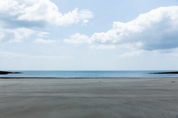 Wide wet sand shoreline is stretching in flat design, with calm sea, cloudy sky, rocky outcroppings