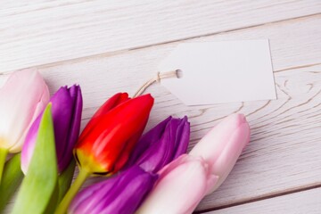 Flat design showing diagonal pink, purple and red tulips on whitewashed planks with blank gift tag
