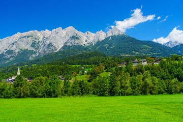 Stunning Austrian landscape featuring a vibrant green meadow, a quaint village surrounded by lush...