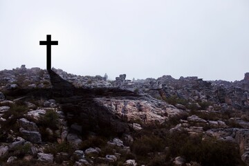 Dark cross silhouette is standing on rugged rocky hilltop in flat design style under overcast sky