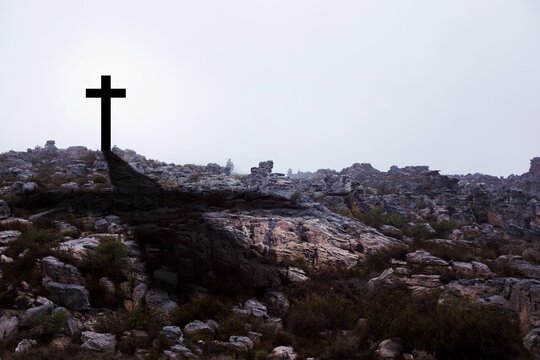 Fototapeta Dark cross silhouette is standing on rugged rocky hilltop in flat design style under overcast sky