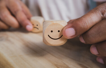 Hand holding wood cube with smile icon, World mental health day or feedback rating concept, Positive customer review, Wood cube stacking with emotion face icon on wood background