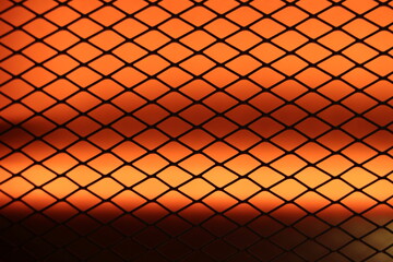 A dark mesh pattern set against a vibrant orange backdrop, generating a sense of warmth, texture,...