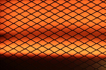 A dark mesh pattern set against a vibrant orange backdrop, generating a sense of warmth, texture,...