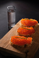 Three sandwiches with red caviar on a saucer on wooden plate. Gourmet appetizer of trout caviar on...