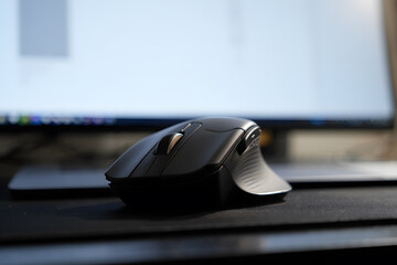 Ergonomic black mouse sitting on a dark mousepad with a blurred screen behind