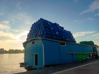 A traditional Indonesian wooden boat that modified barge, heavily laden with a towering pyramid of plastic drums