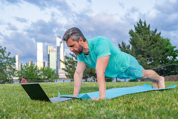 Online sport. Man online workout on yoga mat outdoor. Sport man training with online fitness video....