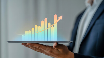 A professional business photo of a hand holding a glowing holographic bar graph visualization floating above a tablet device