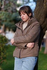 portrait of a teenage girl in a spring park, stands leaning against a tree