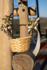 A woven basket adorned with flowers and ribbons hangs on a wooden structure in a serene outdoor setting, capturing a moment of beauty and nature's elegance.