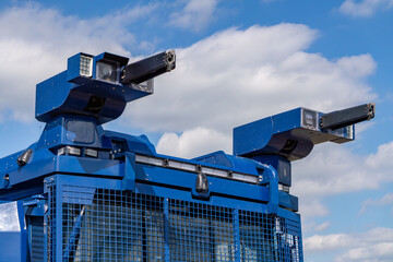 Riot control vehicle turret with water cannons and spotlights mounted on armored police truck against blue sky © Adam