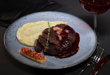 red wine sauce tenderloin served with smashed potatoes with onions, blue plate and black background
