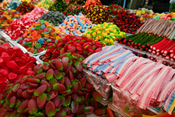 A vibrant assortment of colorful gummy candies and sugary treats at a market stand, illustrating...