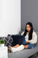 Young adult woman with leg in cast due to fracture and disability uses her laptop to work from home